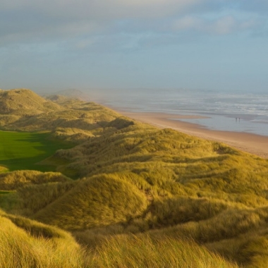 Image of golf green, grassy dunes and sandy beach with ocean